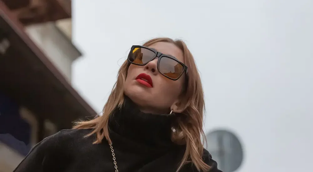 Visão de baixo de mulher com óculos de sol de luxo, batom vermelho e roupas pretas olhando para cima