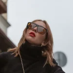Visão de baixo de mulher com óculos de sol de luxo, batom vermelho e roupas pretas olhando para cima