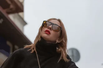 Visão de baixo de mulher com óculos de sol de luxo, batom vermelho e roupas pretas olhando para cima