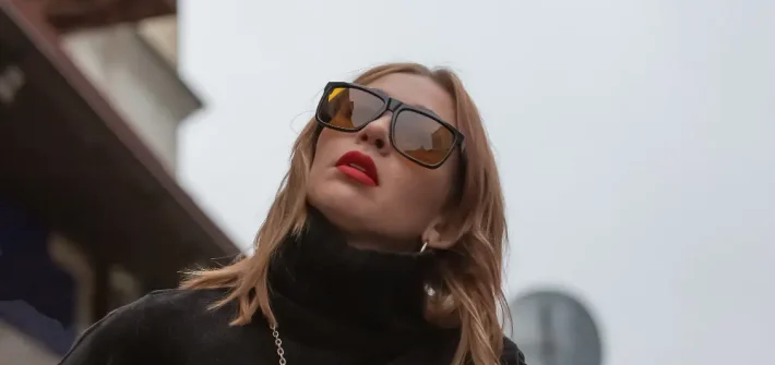 Visão de baixo de mulher com óculos de sol de luxo, batom vermelho e roupas pretas olhando para cima