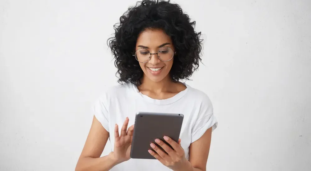 Mulher com óculos de descanso sorrindo enquanto segura e lê em tablet em fundo branco