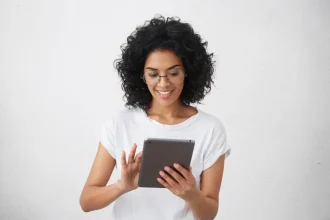 Mulher com óculos de descanso sorrindo enquanto segura e lê em tablet em fundo branco
