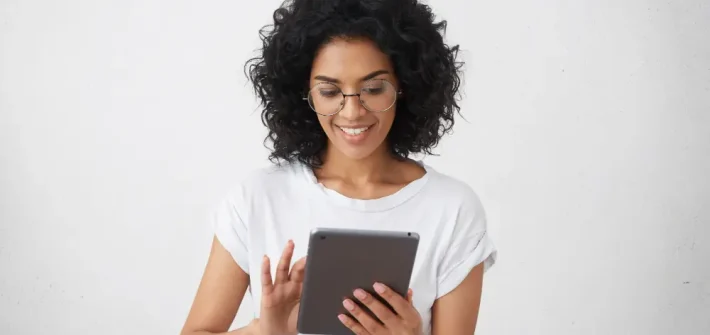 Mulher com óculos de descanso sorrindo enquanto segura e lê em tablet em fundo branco