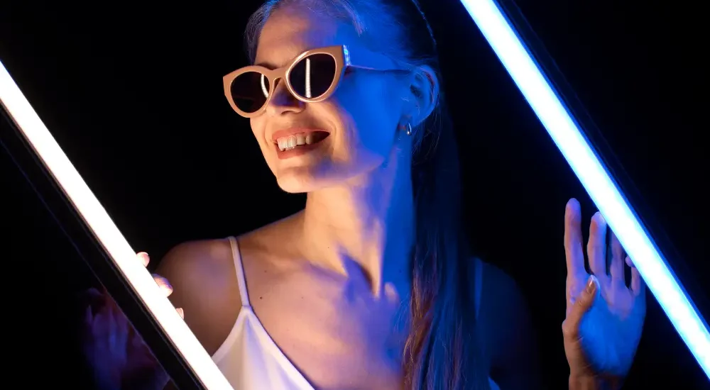 Mulher com óculos de festa de luxo em fundo preto iluminada com luz neon azul