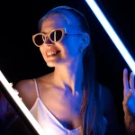 Mulher com óculos de festa de luxo em fundo preto iluminada com luz neon azul