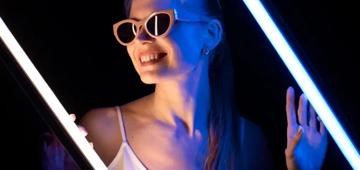 Mulher com óculos de festa de luxo em fundo preto iluminada com luz neon azul