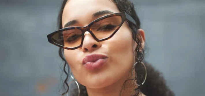 Mulher usando óculos de armação gatinho cor marrom fazendo pose de bico para a foto
