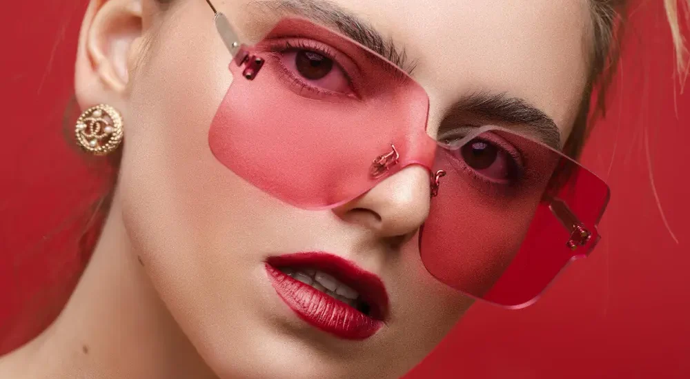 Mulher de maquiagem com óculos de lente rosa avermelhada em fundo vermelho