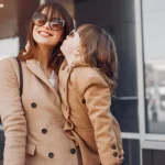 Mãe e filha usando casacos sobretudo e óculos de sol escuro combinando.