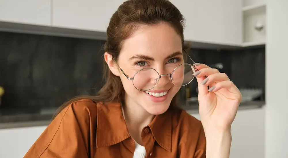 Mulher jovem sorrindo usando óculos de grau estiloso com bancada de cozinha ao fundo em desfoque