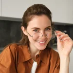 Mulher jovem sorrindo usando óculos de grau estiloso com bancada de cozinha ao fundo em desfoque
