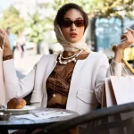 Mulher usando óculos carolina herrera e lenço na cabeça com roupas estilosas e elegantes em mesa ao ar livre
