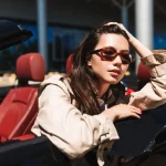 Mulher apoiada na lateral de um carro sem teto com óculos de luxo de sol Ferrari