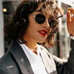 Mulher de lado com óculos de sol Saint Laurent de luxo com sorriso e mão ao lado do rosto
