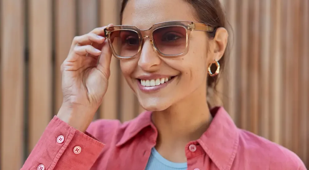 Mulher sorrindo segurando com uma mão com óculos statement no rosto