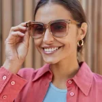 Mulher sorrindo segurando com uma mão com óculos statement no rosto
