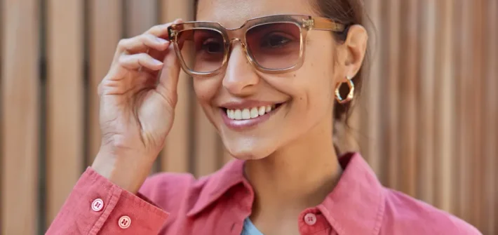 Mulher sorrindo segurando com uma mão com óculos statement no rosto