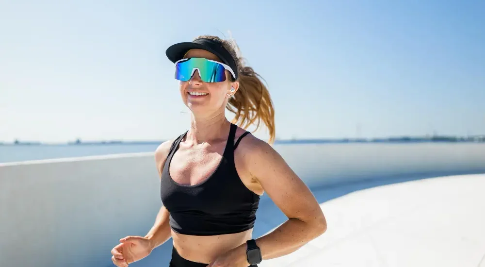 Mulher usando óculos para corrida enquanto corre na praia sorrindo