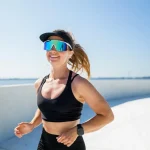 Mulher usando óculos para corrida enquanto corre na praia sorrindo