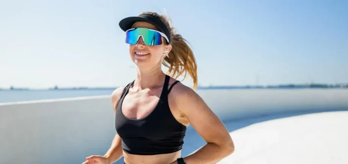 Mulher usando óculos para corrida enquanto corre na praia sorrindo
