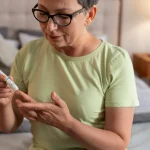 Mulher idosa de óculos com diabete colendo sangue para medir nível de glicose no sangue