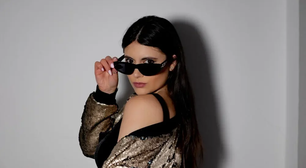 Mulher com óculos e maquiagem olhando para a câmera de lado