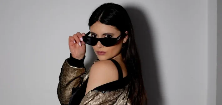 Mulher com óculos e maquiagem olhando para a câmera de lado