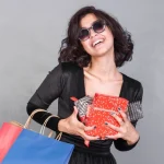 Mulher com óculos de sol de luxo sorrindo segurando presentes de amigo secreto