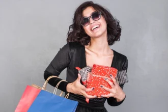 Mulher com óculos de sol de luxo sorrindo segurando presentes de amigo secreto