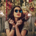 Mulher com óculos escuro no ano novo segurando vela faísca