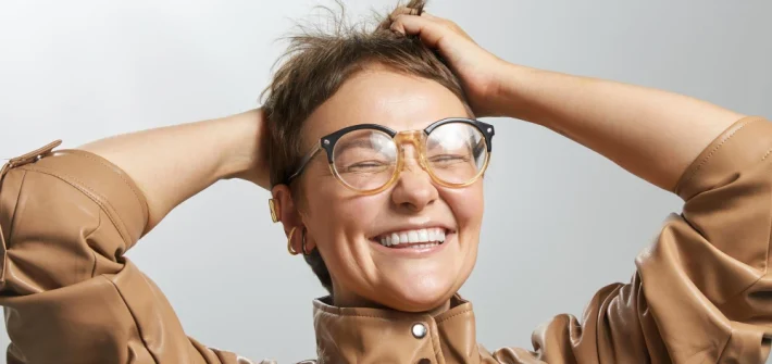 Mulher usando óculos original de grau e sorrindo com as duas mãos no cabelo