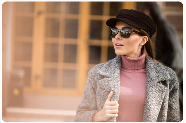 Mulher elegante em trajes de inverno usa óculos Tom Ford original e boina preta, posando em frente a uma fachada clássica.